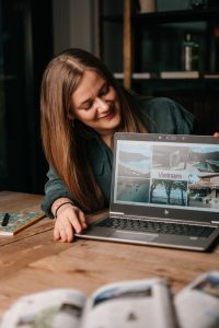 Frau sitzt am Tisch und hält ihren Laptop geöffnet, auf dem verschiedene Urlaubsbilder mit dem Schriftzug „Vietnam“ zu sehen sind.
