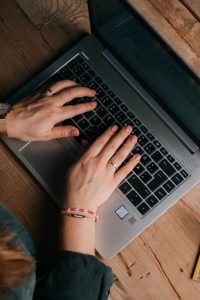 Obere Ansicht von zwei Händen, die auf der Tastatur eines Laptops schreiben.